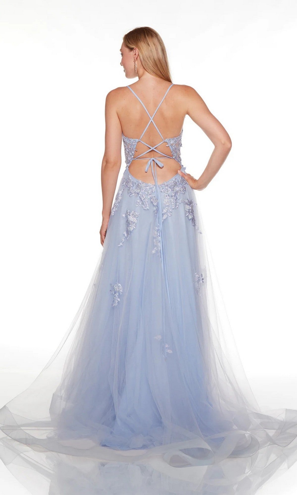 A woman stands facing away, wearing the Alyce 61263 long formal dress—a light blue gown with lace appliques, thin crisscross straps, and a flowing tulle skirt.